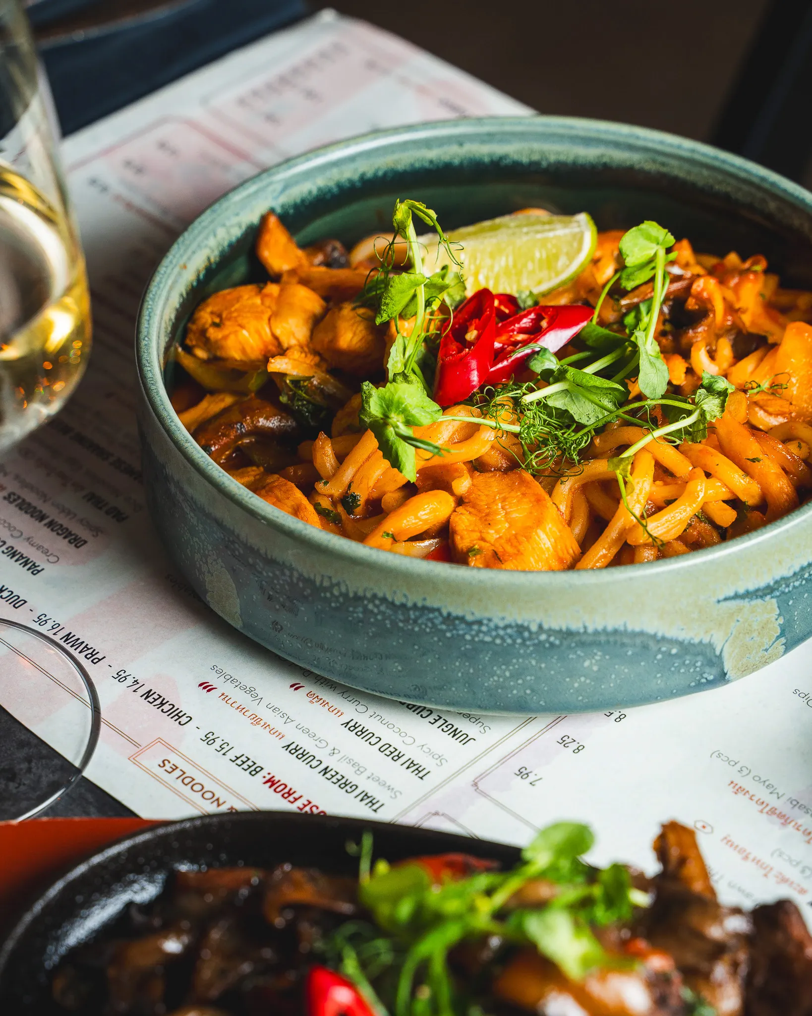 A bowl of noodles with fresh herbs, red chilli and lime.