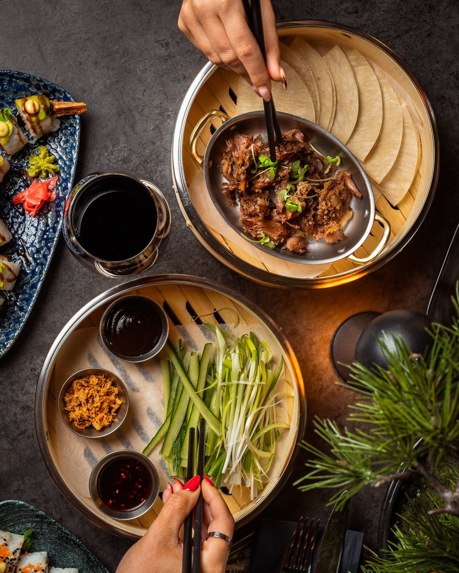 An overhead view of guests sharing pancakes, cucumber, spring onions and a meat dish.