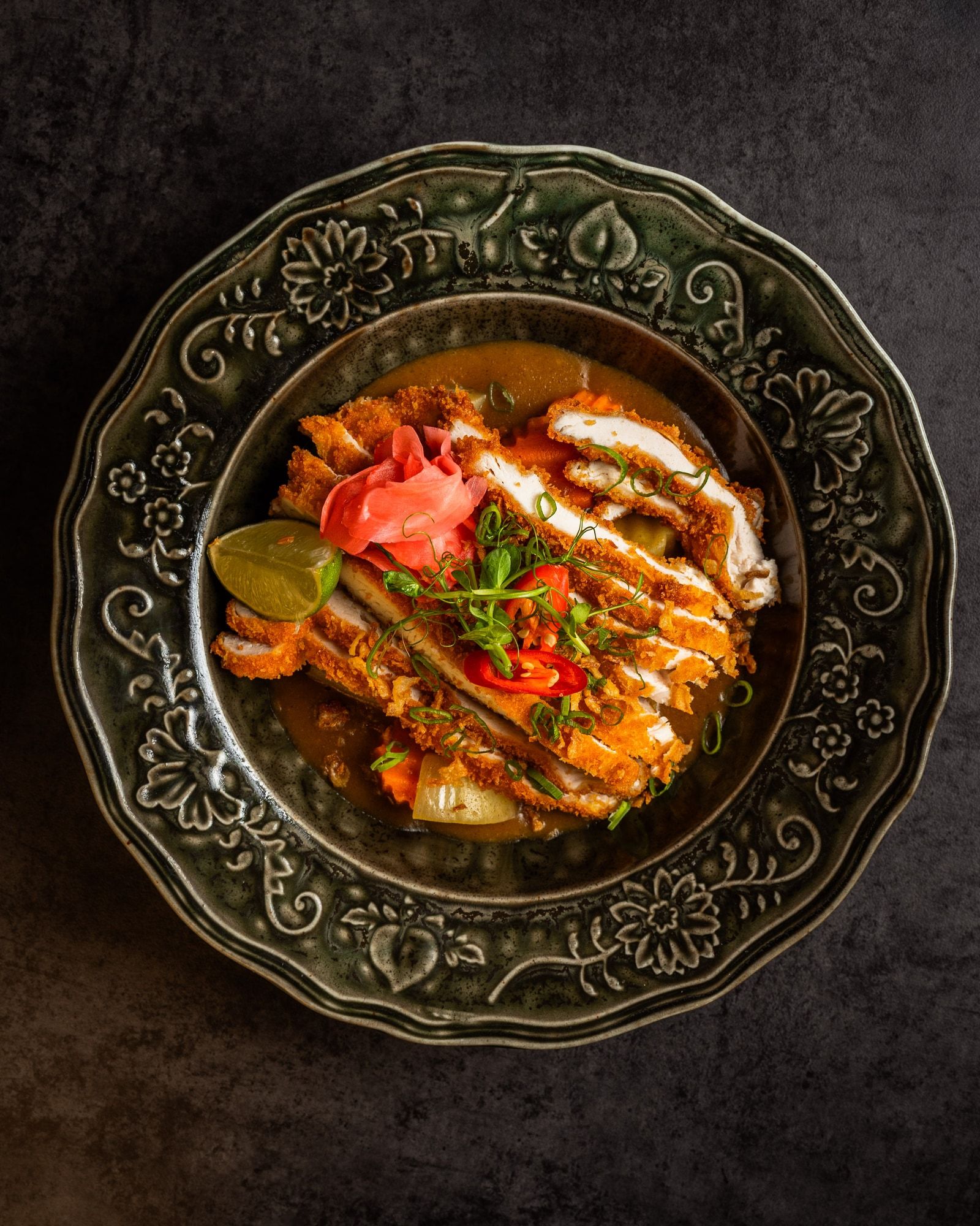 Sliced breaded chicken over curry sauce, garnished with chilli and pickled ginger.