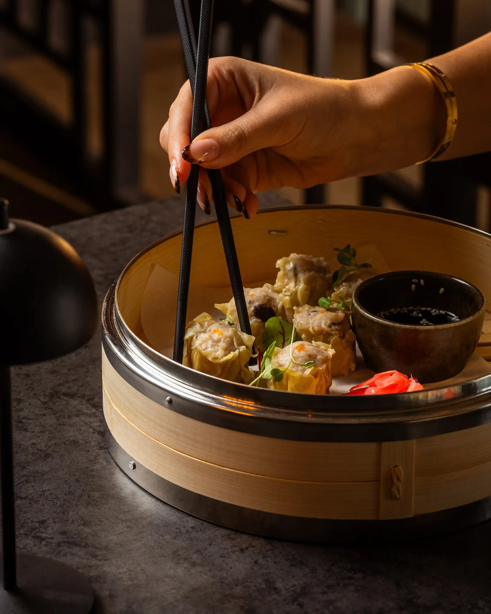 A guest choosing dim sum from a bamboo steamer with chopsticks.