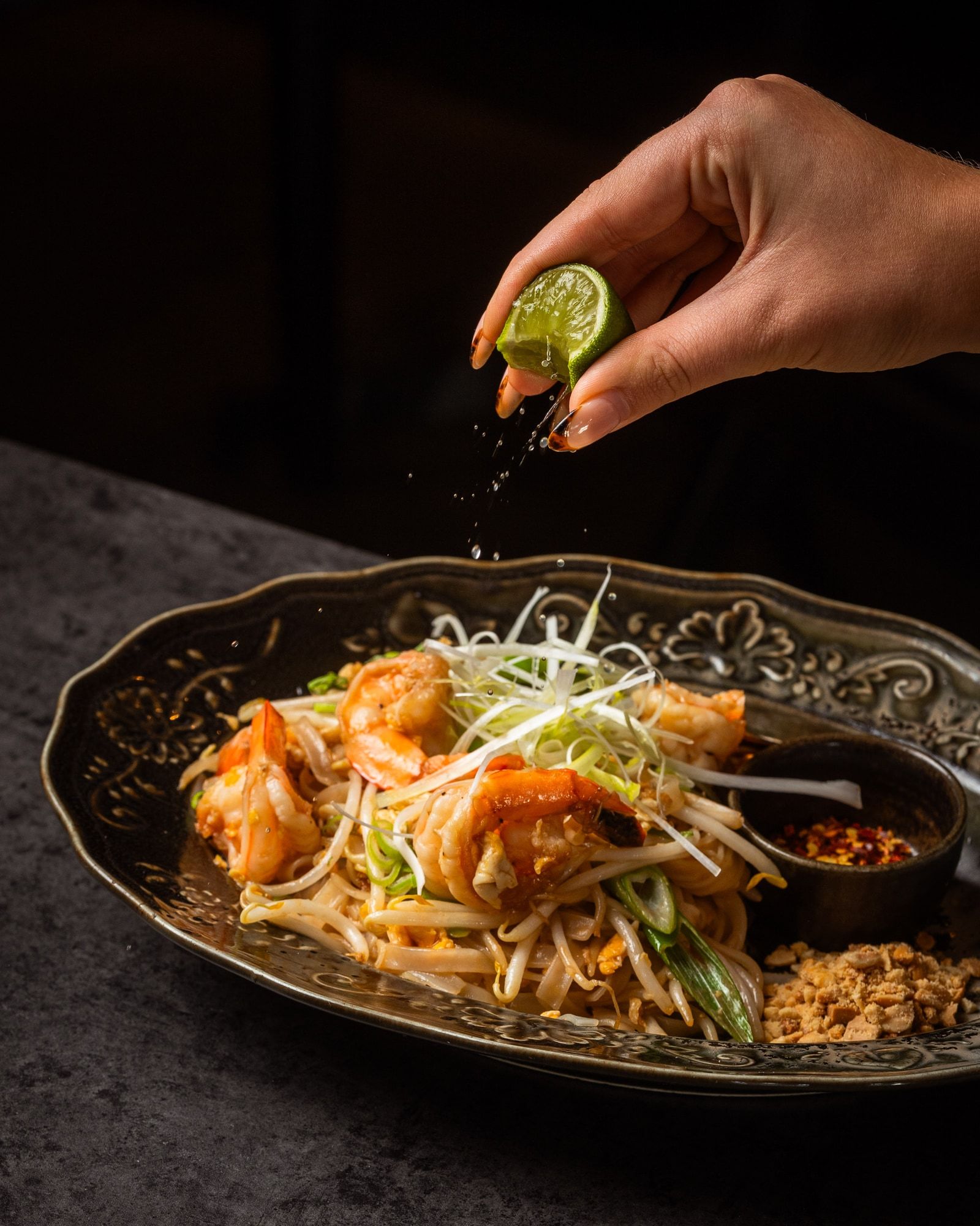 A guest squeezing lime over a plate of prawn noodles.
