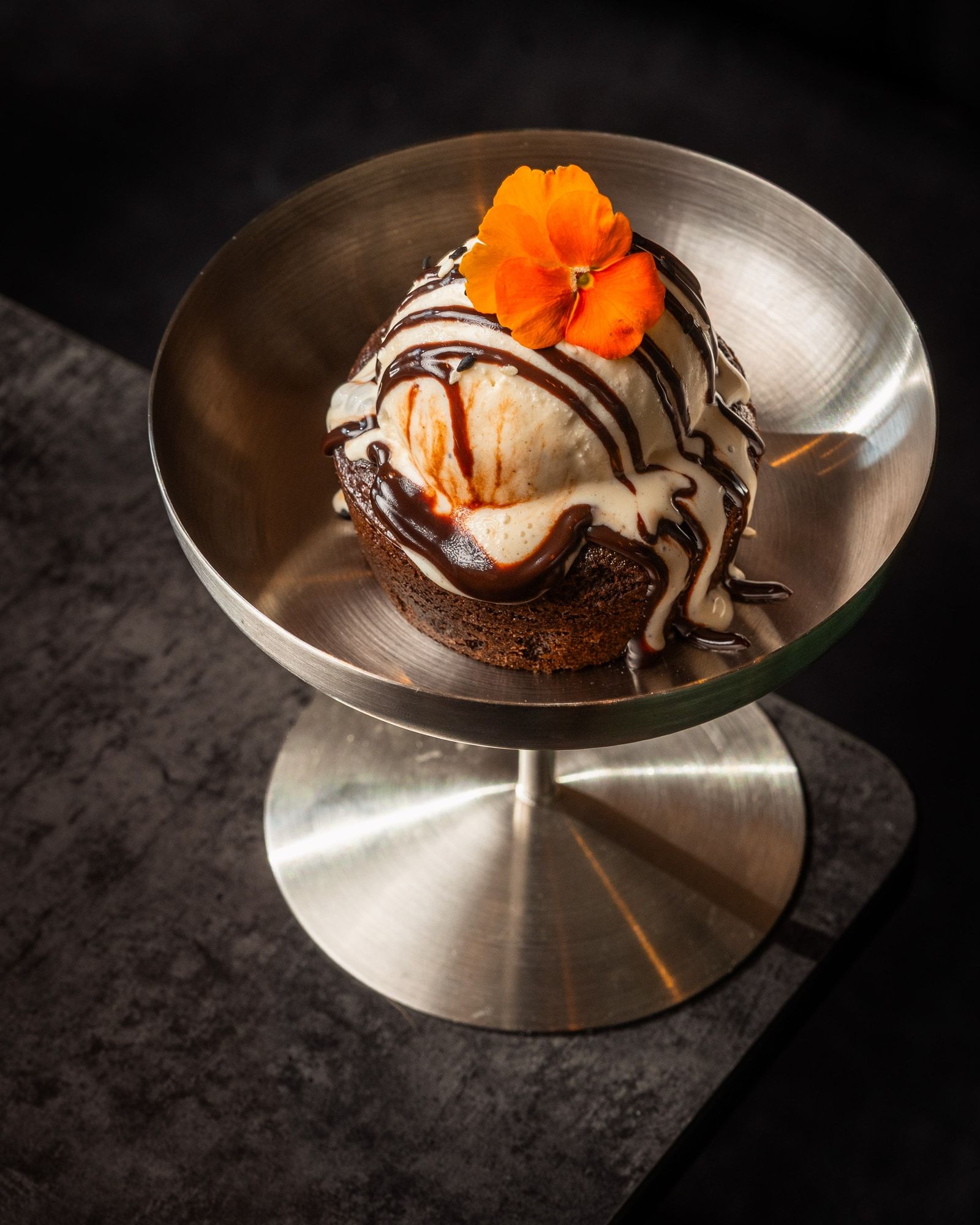 A chocolate dessert with ice cream, chocolate sauce and an edible flower.
